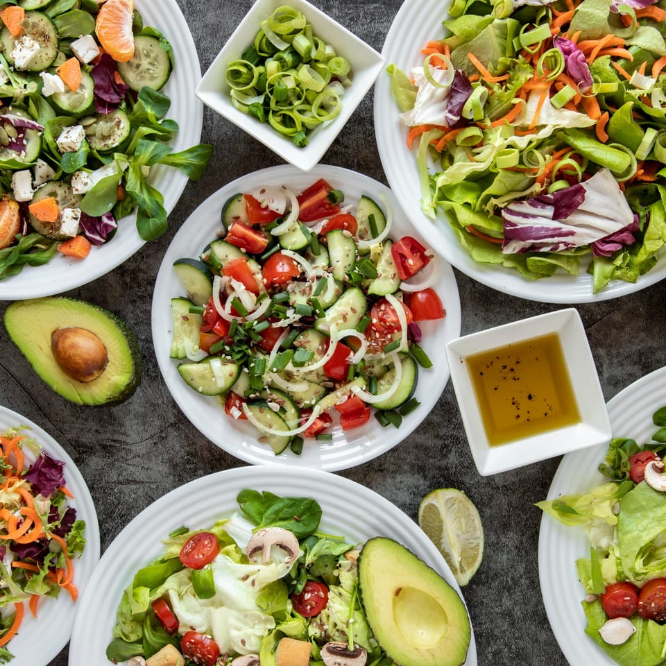 Overhead view of various fresh salads, including cucumber, tomato, avocado, and mixed greens.