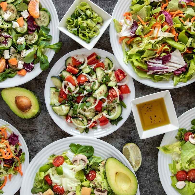 Overhead view of various fresh salads, including cucumber, tomato, avocado, and mixed greens.