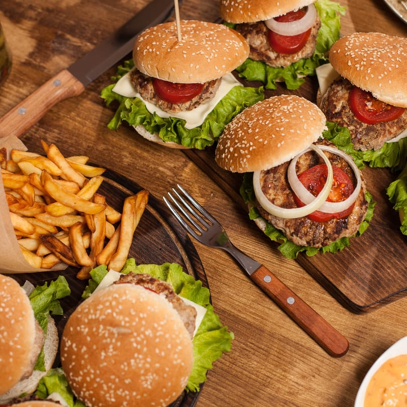 Several burgers with lettuce, tomato, onion, and cheese, alongside fries and a dipping sauce.