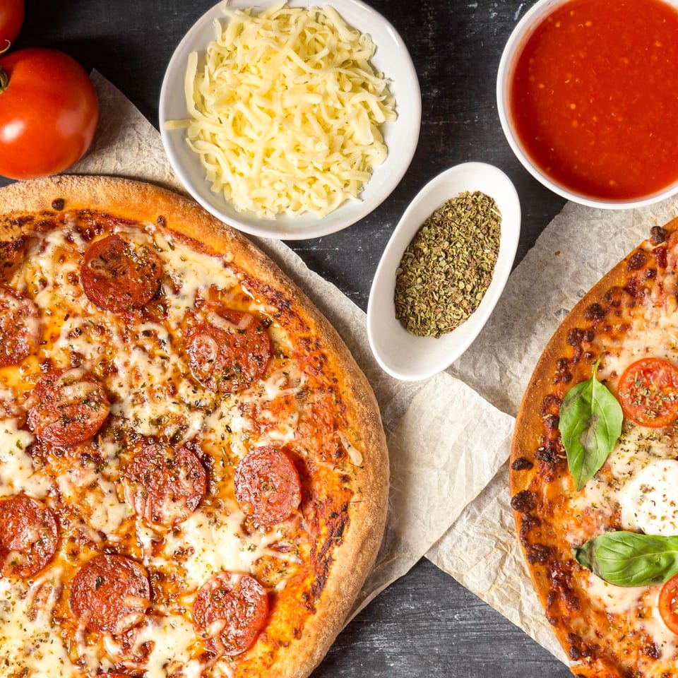 Two pizzas, one pepperoni and one Margherita, with ingredients like cheese, sauce, and herbs.
