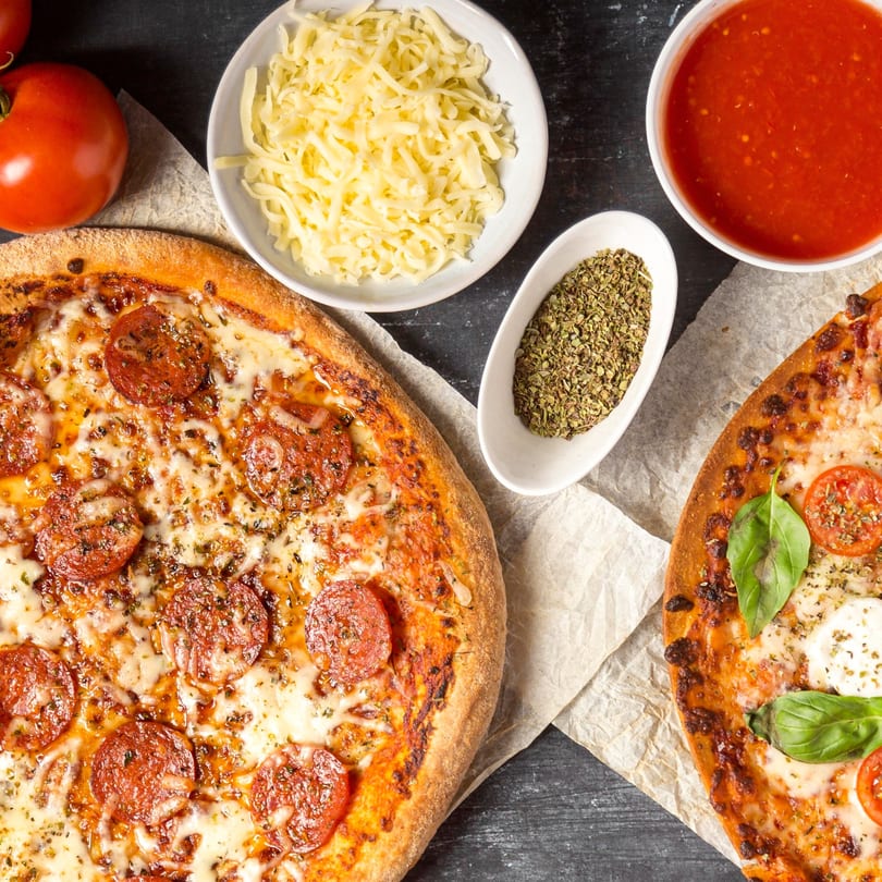 Two pizzas, one pepperoni and one Margherita, with ingredients like cheese, sauce, and herbs.