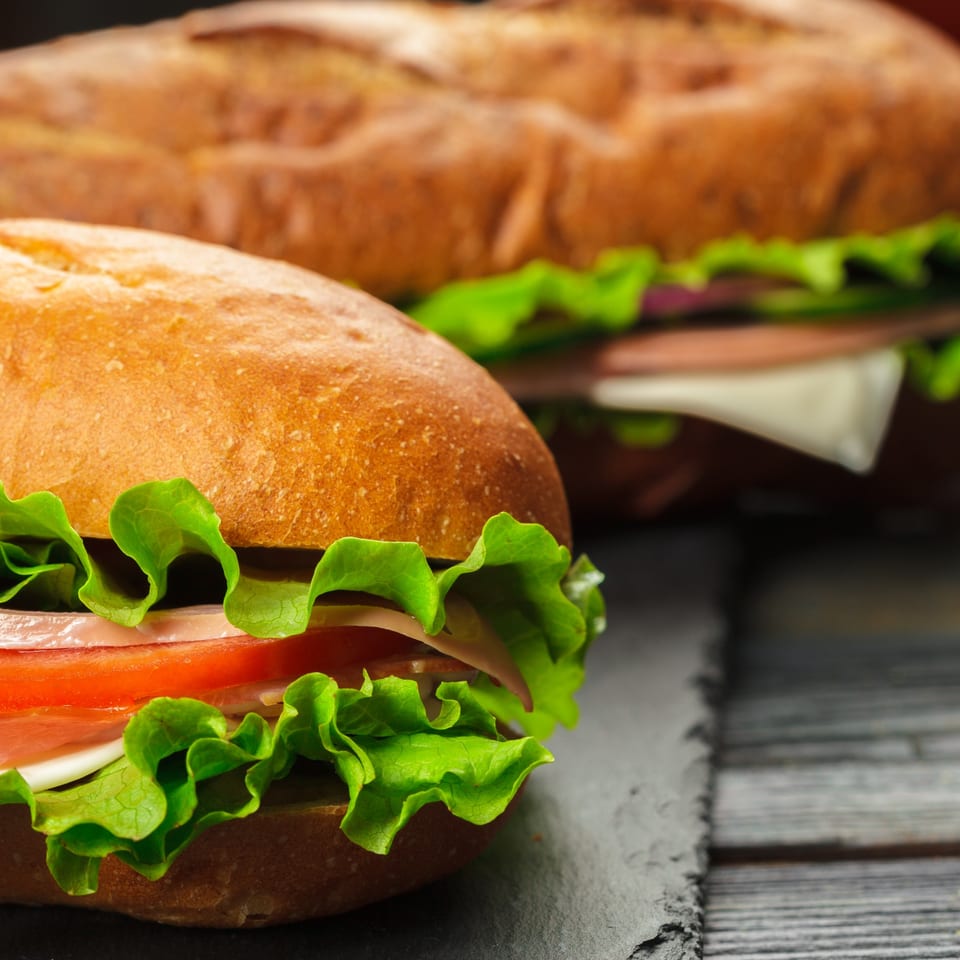 Two fresh sandwiches with lettuce, tomato, and cheese on a dark wooden surface.