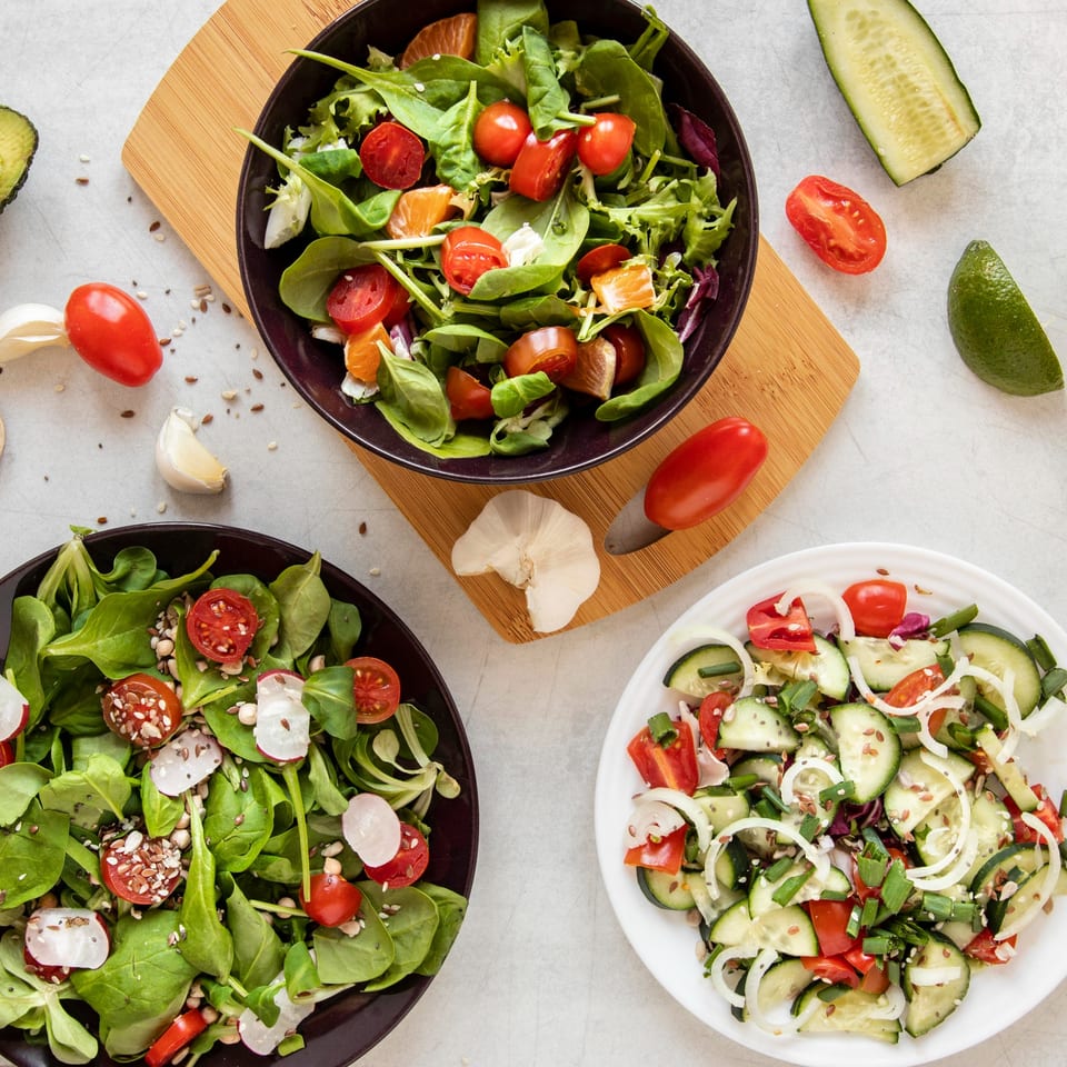 Three bowls of fresh salads with various vegetables, including tomatoes, cucumbers, and leafy greens.